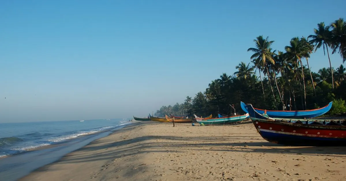 Fishing boats lined up on the serene beach of Alleppey, Kerala, with coconut trees and calm blue sea under a clear sky  a peaceful morning in God’s Own Country.